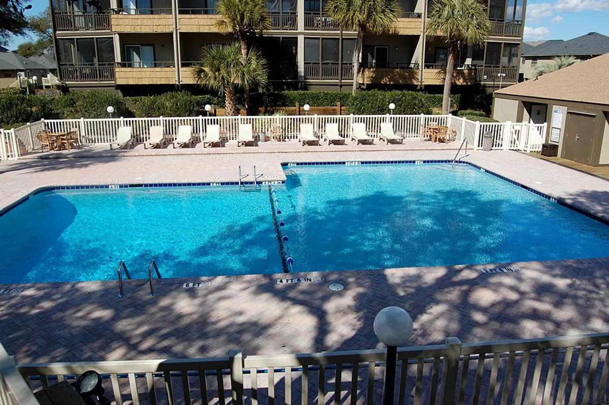 The image highlights a serene swimming pool surrounded by lounge chairs and palm trees, capturing a tranquil moment with the sun setting behind the pool. The inviting water and lush greenery create a resort-like atmosphere, ideal for relaxation or socializing with neighbors.