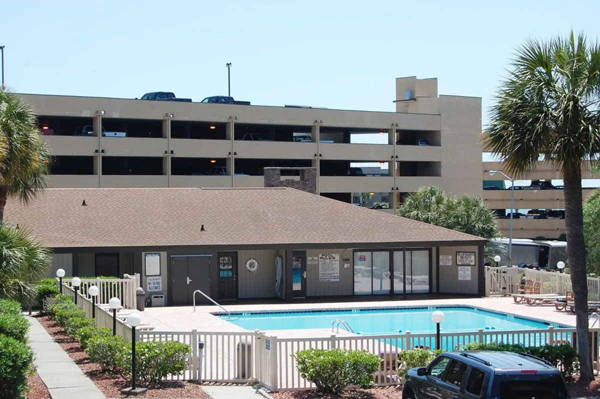 An inviting exterior view of the swimming pool and lounge area surrounded by palm trees and Mariner's Cove buildings. The scene is tranquil, with spaces for socializing or relaxing under the mild Myrtle Beach winter sun.