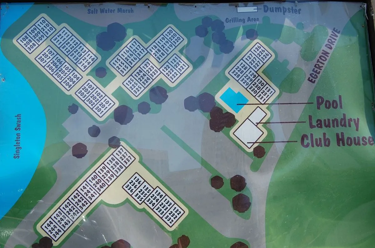 This exterior image features the community pool area, the clubhouse, a laundry facility, and a grilling area. You can see residents socializing near the pool, with the clubhouse in the background, setting the scene for both relaxation and community events. The pool is bordered by lounge chairs and surrounded by well-maintained landscaping.